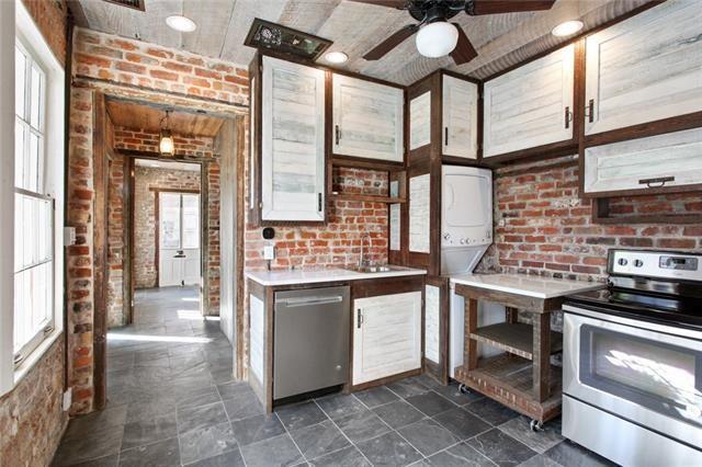 941-943 Toulouse St, New Orleans, LA 70112 - kitchen with stainless steel appliances, stacked washing machine and dryer, brick wall, light countertops, and ceiling fan