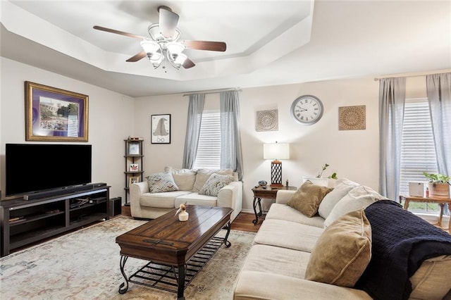 living room featuring plenty of natural light, ceiling fan, a raised ceiling, and light hardwood / wood-style flooring