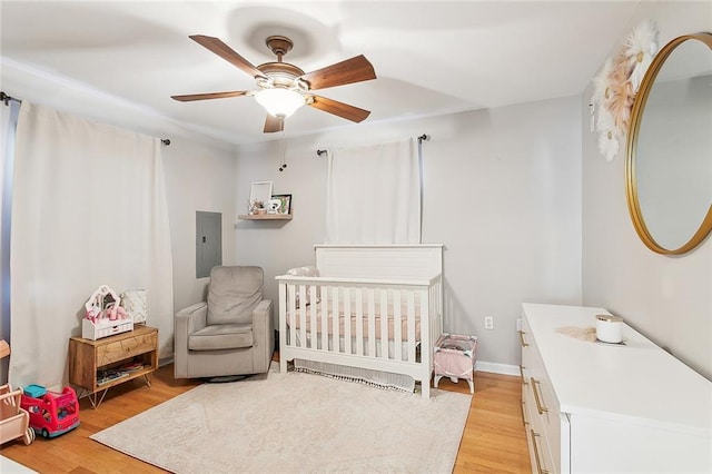 bedroom featuring electric panel, ceiling fan, a nursery area, and light wood-type flooring