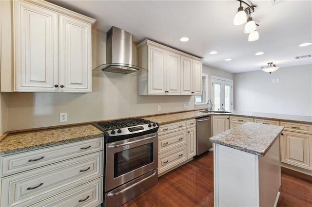 kitchen with sink, wall chimney exhaust hood, light stone countertops, appliances with stainless steel finishes, and a kitchen island