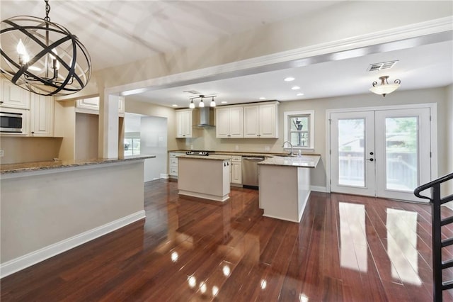 kitchen featuring light stone countertops, wall chimney exhaust hood, hanging light fixtures, an inviting chandelier, and appliances with stainless steel finishes