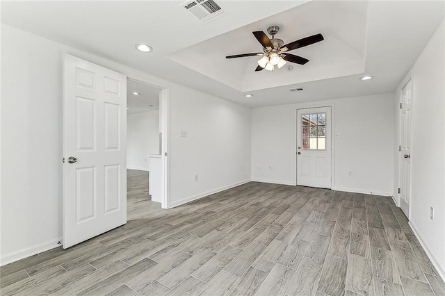 unfurnished room with light hardwood / wood-style floors, a raised ceiling, and ceiling fan