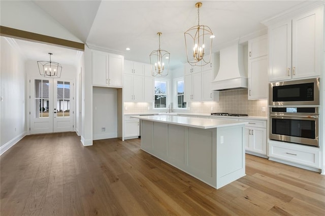 kitchen with white cabinets, decorative light fixtures, custom exhaust hood, and stainless steel oven