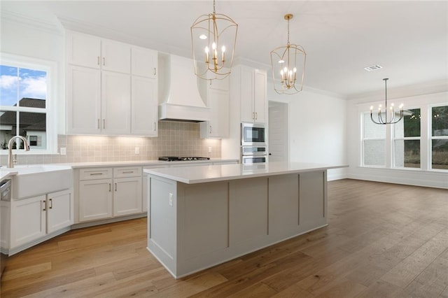 kitchen with premium range hood, sink, white cabinets, and a kitchen island