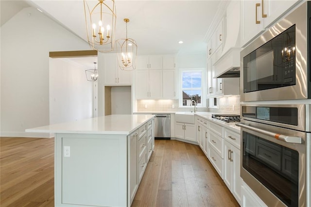 kitchen featuring backsplash, stainless steel appliances, decorative light fixtures, white cabinets, and a center island