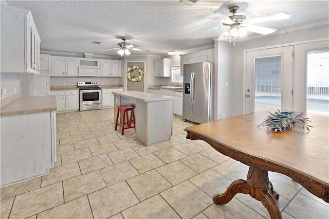 kitchen featuring stainless steel appliances, a kitchen bar, white cabinets, and light countertops