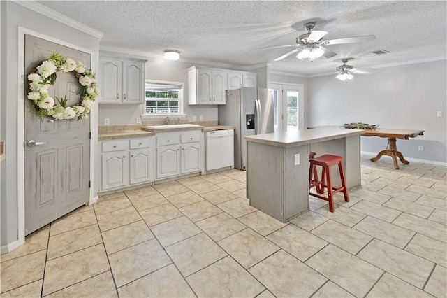 kitchen featuring a kitchen bar, light countertops, stainless steel refrigerator with ice dispenser, white dishwasher, and a sink