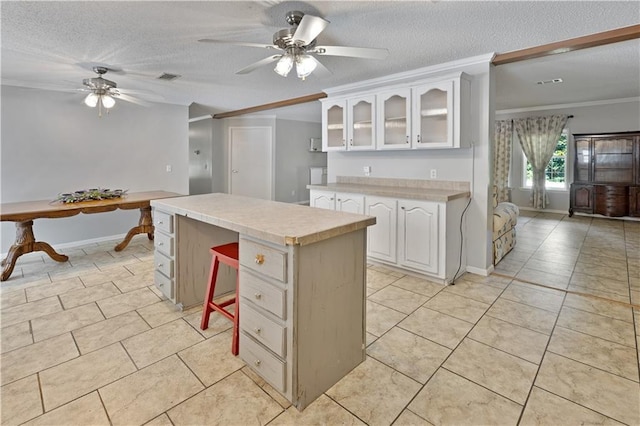 kitchen with a kitchen island, ornamental molding, light countertops, glass insert cabinets, and a textured ceiling