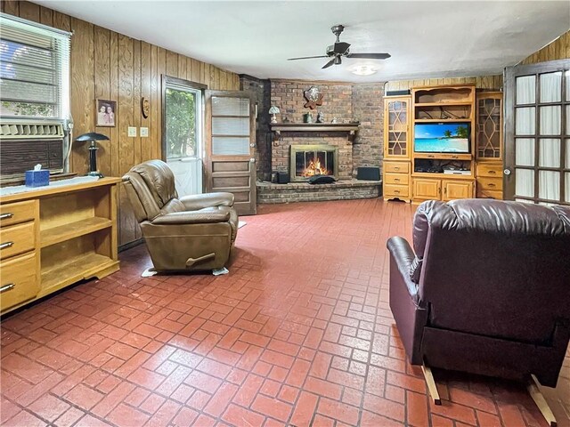 living room featuring ceiling fan, wooden walls, and a brick fireplace