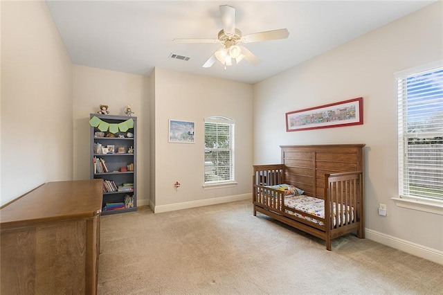 bedroom with ceiling fan, light colored carpet, and a crib