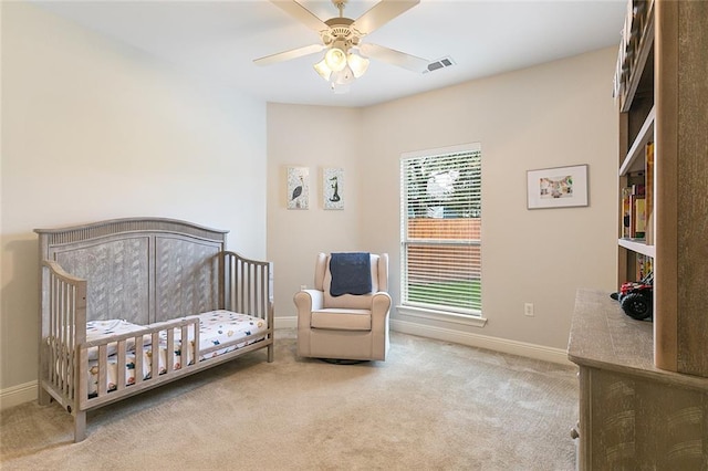 carpeted bedroom with multiple windows, ceiling fan, and a crib