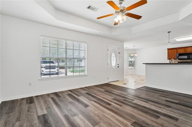 unfurnished living room with a tray ceiling, dark hardwood / wood-style floors, and a healthy amount of sunlight