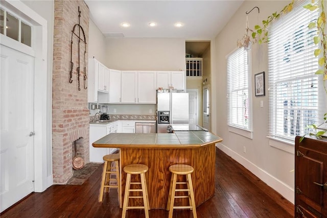 kitchen featuring tile countertops, a breakfast bar, dark wood-type flooring, white cabinets, and stainless steel appliances