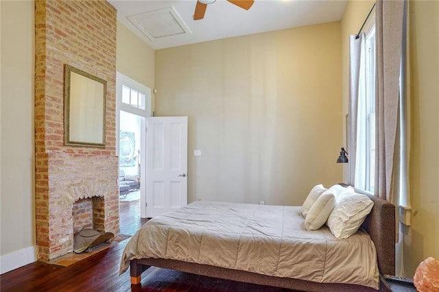 bedroom with multiple windows, ceiling fan, wood-type flooring, and a brick fireplace