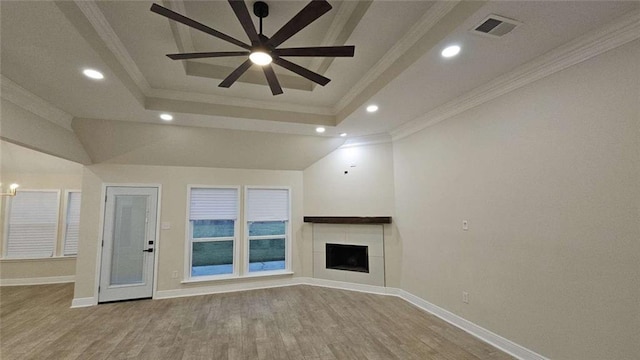 unfurnished living room with crown molding, light hardwood / wood-style flooring, ceiling fan, a tray ceiling, and a tiled fireplace