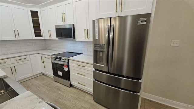 kitchen featuring tasteful backsplash, light stone counters, white cabinetry, and appliances with stainless steel finishes