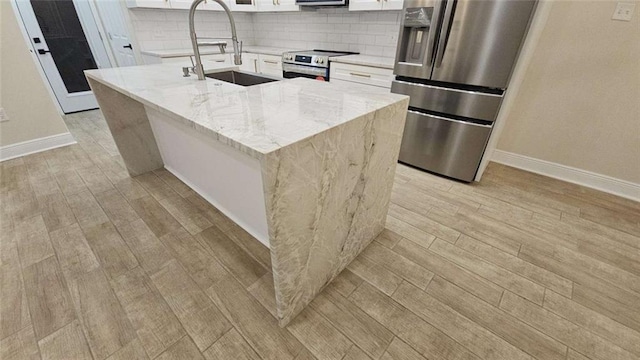 kitchen with appliances with stainless steel finishes, light stone counters, sink, white cabinets, and an island with sink