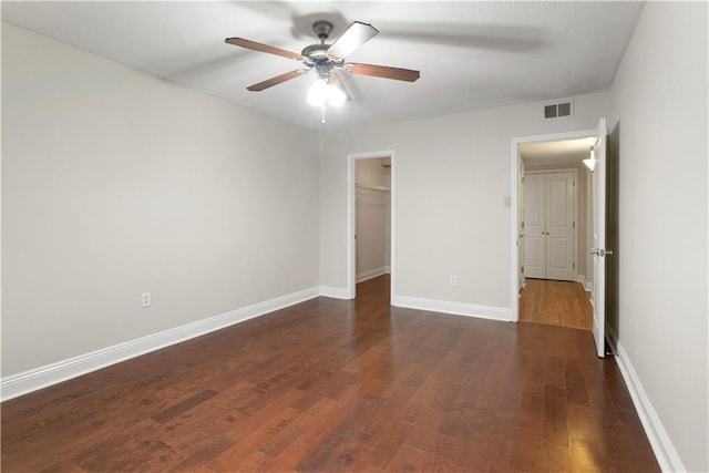 unfurnished bedroom featuring a closet, a walk in closet, dark hardwood / wood-style floors, and ceiling fan