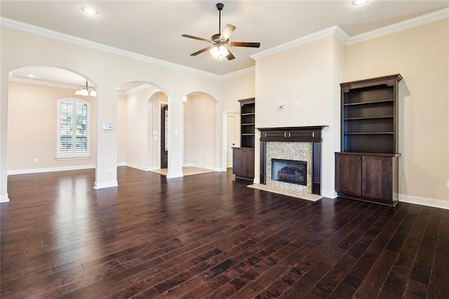 unfurnished living room featuring ceiling fan with notable chandelier, dark hardwood / wood-style flooring, a stone fireplace, and ornamental molding