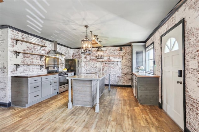 kitchen featuring stainless steel appliances, wall chimney range hood, brick wall, gray cabinets, and ornamental molding