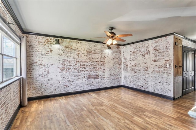 unfurnished room featuring wood-type flooring, ceiling fan, crown molding, and brick wall