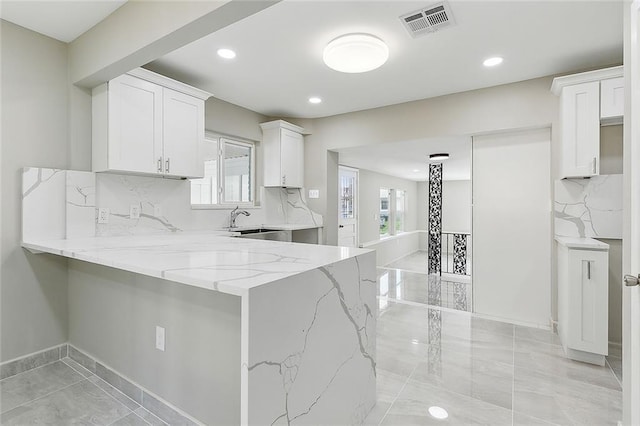 kitchen featuring white cabinetry, sink, backsplash, light stone counters, and kitchen peninsula