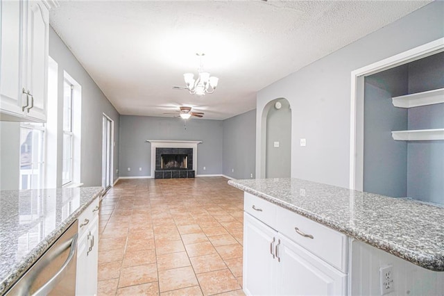 kitchen with a tile fireplace, white cabinetry, light stone counters, stainless steel dishwasher, and ceiling fan with notable chandelier