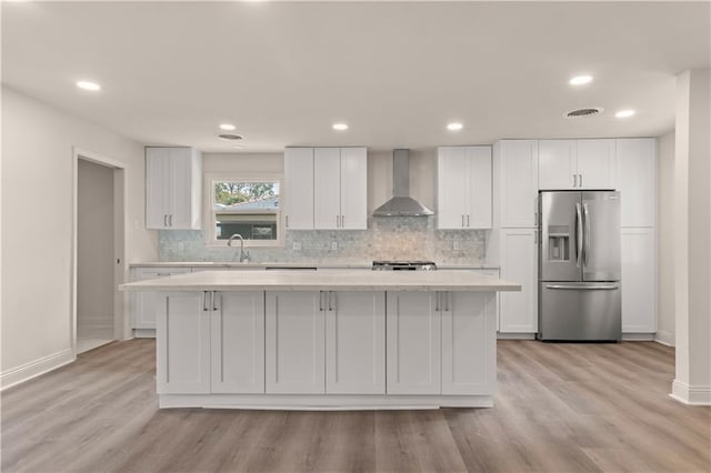 kitchen featuring white cabinets, stainless steel fridge, wall chimney exhaust hood, and a kitchen island