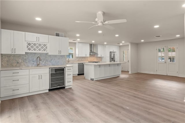 kitchen featuring white cabinets, appliances with stainless steel finishes, wall chimney range hood, and beverage cooler