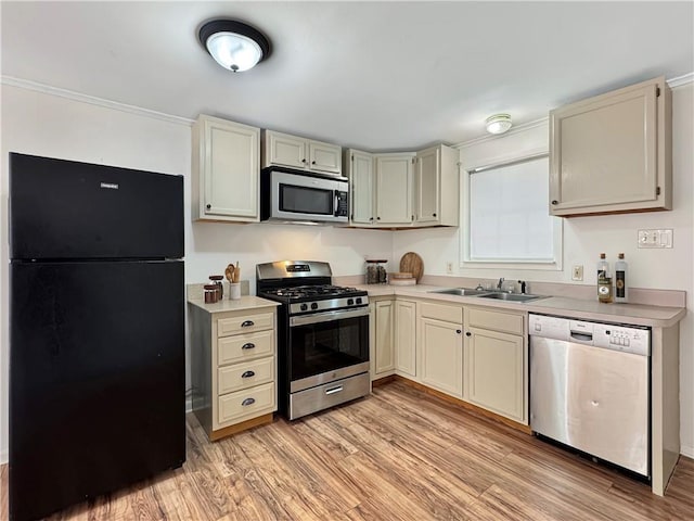 kitchen with appliances with stainless steel finishes, light wood-type flooring, cream cabinets, and sink