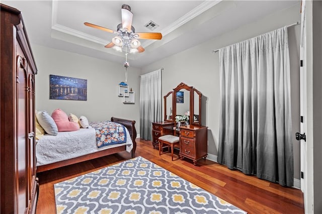 bedroom featuring hardwood / wood-style flooring, ceiling fan, crown molding, and a tray ceiling