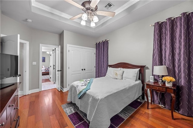 bedroom featuring wood-type flooring, a raised ceiling, ceiling fan, and crown molding