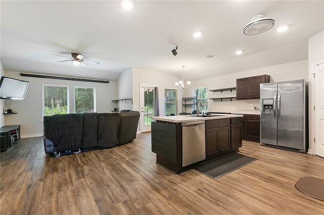 kitchen featuring appliances with stainless steel finishes, light wood-type flooring, decorative light fixtures, and an island with sink