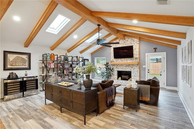 living room featuring a stone fireplace, ceiling fan, vaulted ceiling with skylight, and light hardwood / wood-style flooring