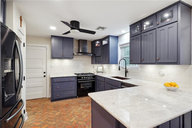 kitchen with stainless steel fridge with ice dispenser, kitchen peninsula, black gas range oven, and wall chimney range hood