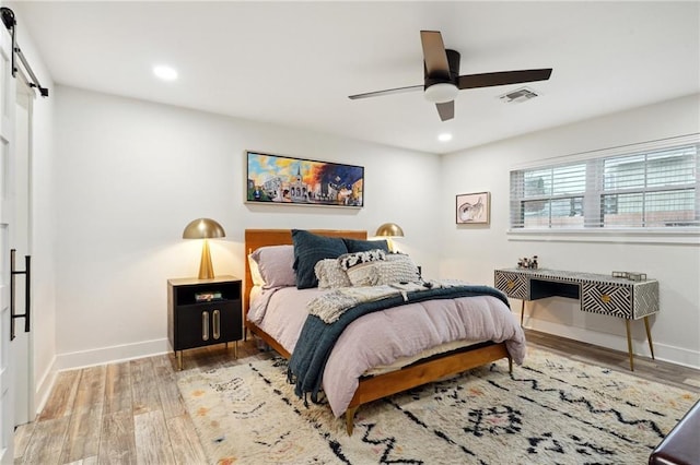 bedroom with a barn door, ceiling fan, and wood-type flooring