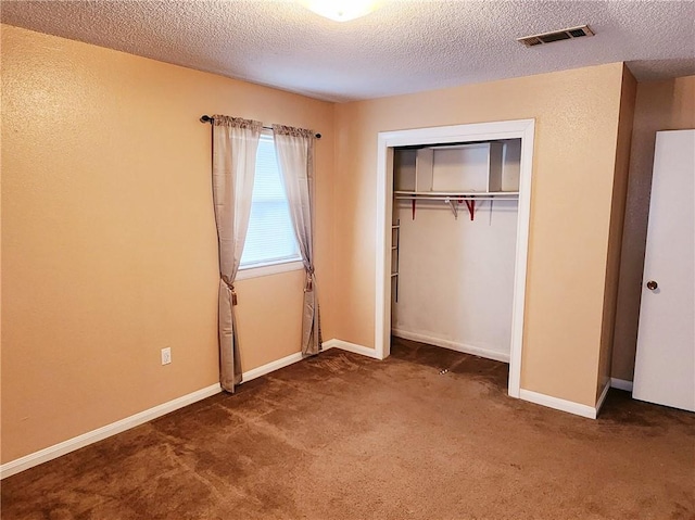 unfurnished bedroom featuring a textured ceiling, dark carpet, and a closet