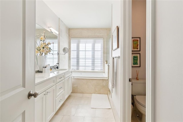 bathroom with tile patterned flooring, vanity, tiled bath, and toilet