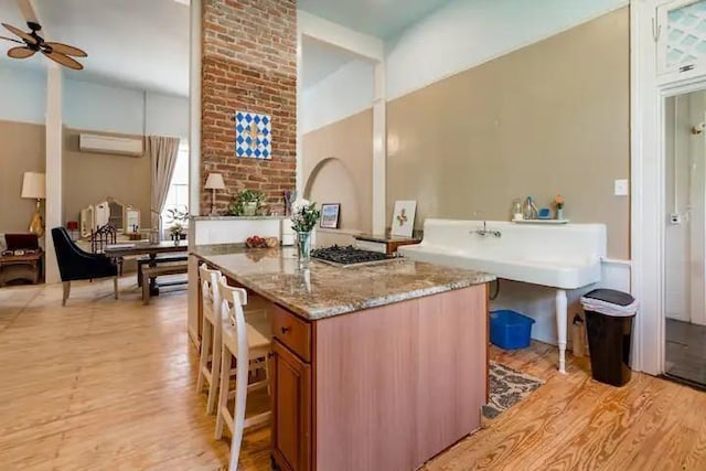 kitchen with a kitchen breakfast bar, ceiling fan, light stone countertops, light wood-type flooring, and a kitchen island