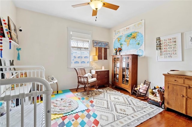 bedroom with ceiling fan, hardwood / wood-style floors, and a crib