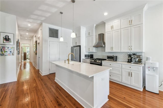 kitchen featuring wall chimney range hood, sink, appliances with stainless steel finishes, decorative light fixtures, and white cabinetry