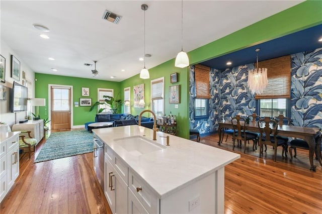 kitchen with sink, hanging light fixtures, a kitchen island with sink, white cabinets, and ceiling fan with notable chandelier