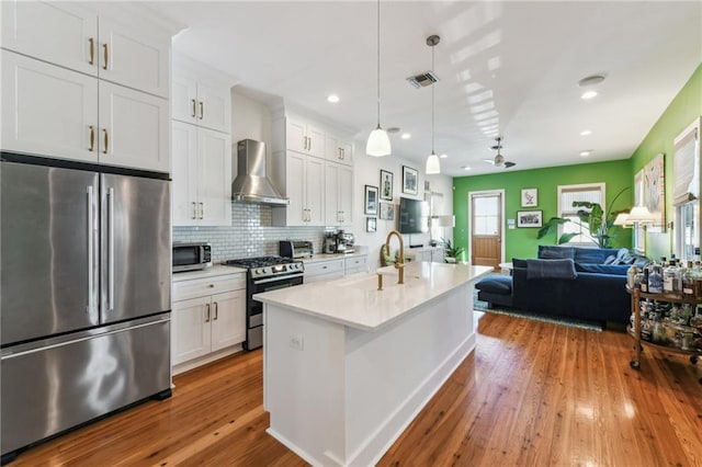 kitchen featuring white cabinetry, sink, wall chimney exhaust hood, hanging light fixtures, and stainless steel appliances