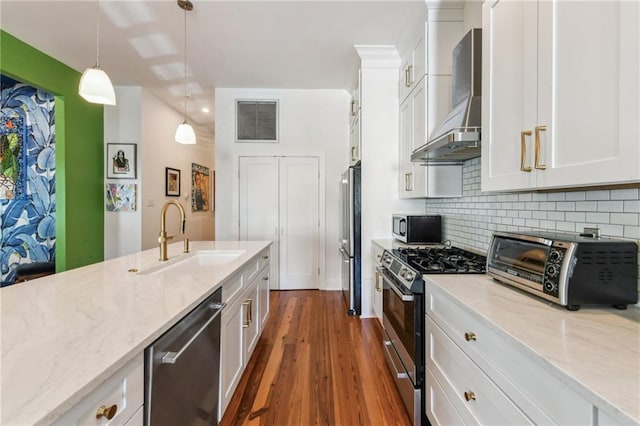 kitchen with sink, wall chimney exhaust hood, hanging light fixtures, stainless steel appliances, and white cabinets