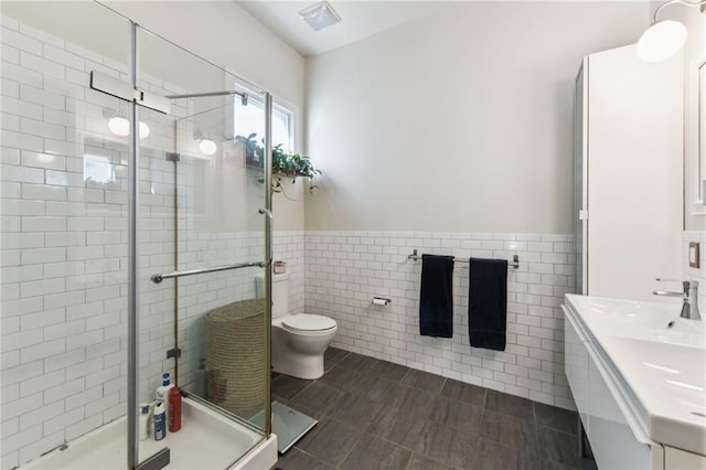 bathroom featuring tile patterned flooring, toilet, vanity, a shower with shower door, and tile walls