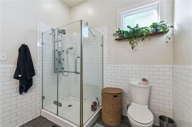 bathroom featuring tile patterned floors, a shower with door, toilet, and tile walls