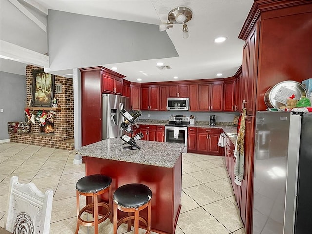 kitchen featuring a kitchen breakfast bar, light tile patterned floors, a kitchen island, light stone counters, and stainless steel appliances