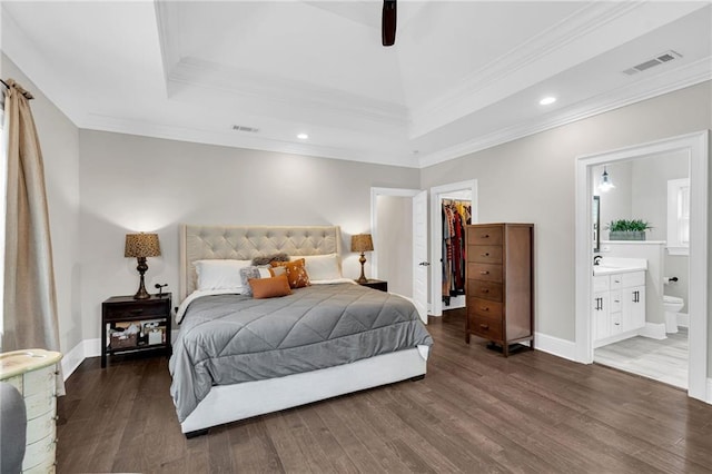 bedroom with a spacious closet, ornamental molding, dark hardwood / wood-style floors, a tray ceiling, and a closet