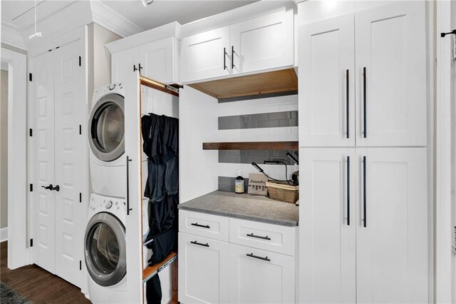 clothes washing area featuring stacked washer / drying machine, dark wood-type flooring, and cabinets