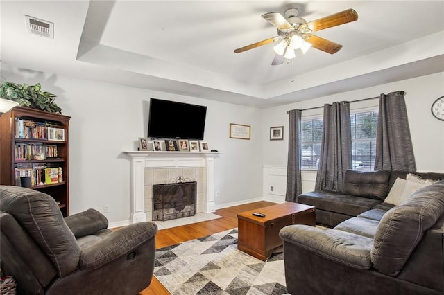 living room featuring a tray ceiling, ceiling fan, light hardwood / wood-style floors, and a tiled fireplace